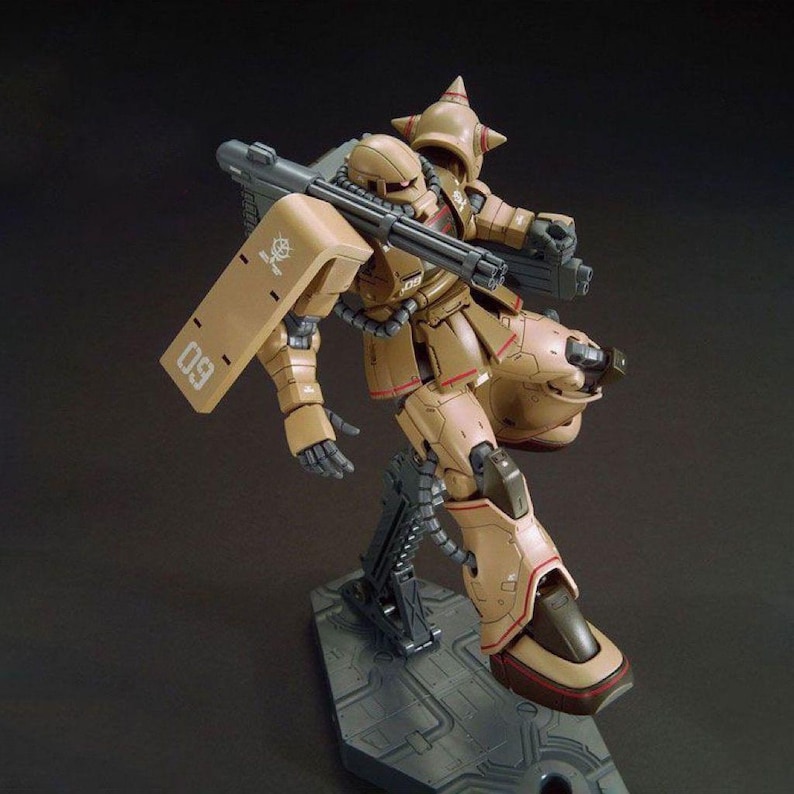 Puede incluir: Un modelo de robot marr&oacute;n y beige con un arma grande y un escudo. El robot est&aacute; posado sobre un soporte gris. El escudo tiene el n&uacute;mero "09" impreso. El robot tiene un casco puntiagudo y m&uacute;ltiples armas.