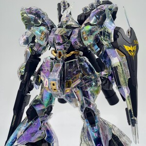 May include: A detailed model of a robot with iridescent, transparent armor. The robot has black and gold accents, including a shield with a gold emblem. The armor reflects a rainbow of colors, including purple, green, and yellow. The model is highly detailed.