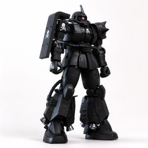 May include: A matte black Zaku robot action figure featuring a mono-eye sensor, a spiked left shoulder armor, and a large rectangular shield on the right arm. The figure is decorated with white skull and crossbones emblems on the shield, chest, and hand.
