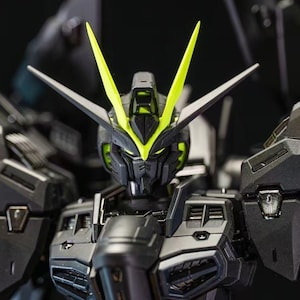 May include: Close-up of a detailed black and gray robot model with neon green accents. The robot has sharp angles, a detailed face, and prominent head crests. The model is a collectible item.