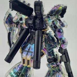 May include: A clear, iridescent model kit of a robot with black and gold accents. The robot has a complex design with multiple articulated parts, including a gun and cylindrical components. The clear plastic allows a view of the internal structure.