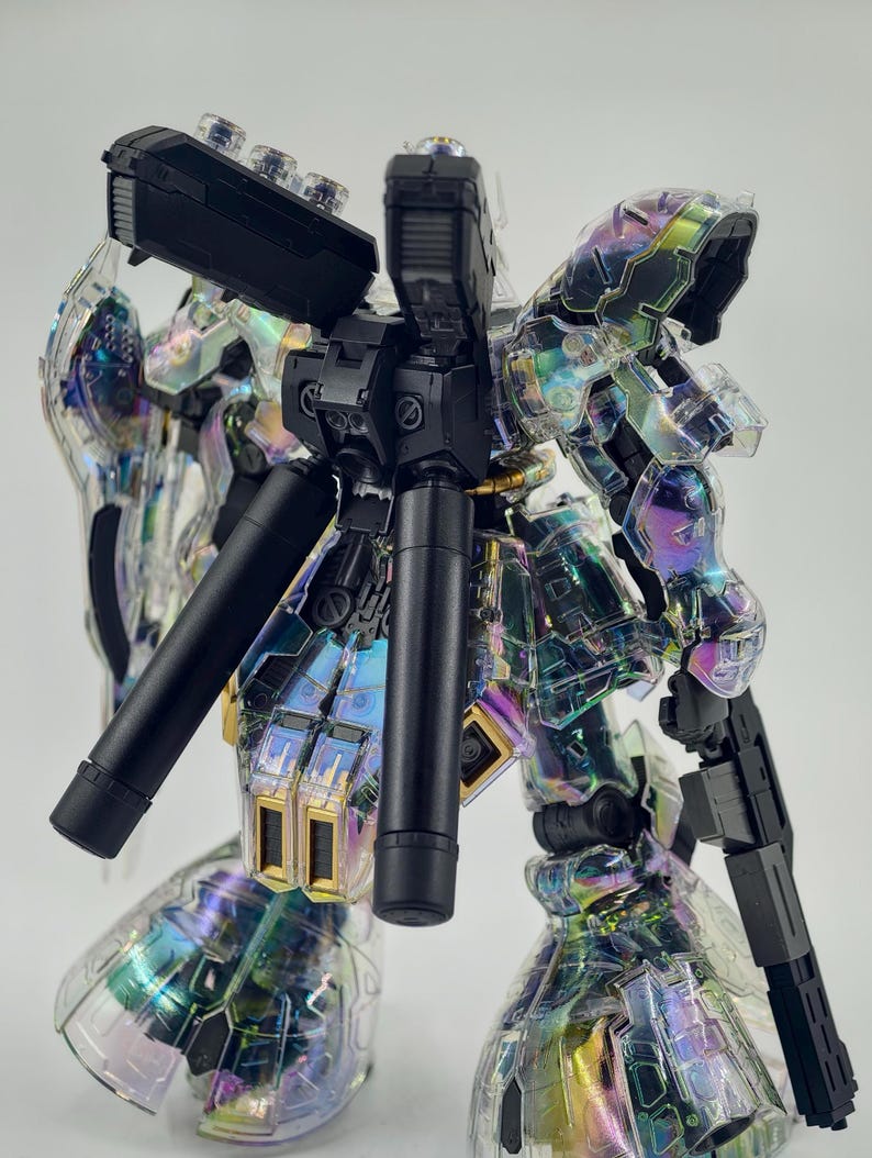 May include: A clear, iridescent model kit of a robot with black and gold accents. The robot has a complex design with multiple articulated parts, including a gun and cylindrical components. The clear plastic allows a view of the internal structure.