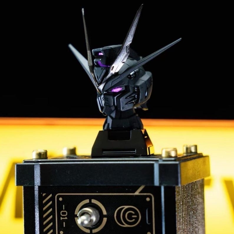 May include: A black robot head with silver accents and purple glowing eyes and details. The head is mounted on a black base with gold-colored hardware. The overall design suggests a futuristic or sci-fi theme.