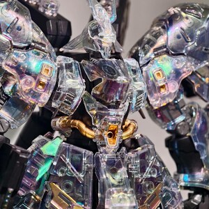 May include: A detailed, clear plastic model of a robot with iridescent accents. The robot features intricate detailing, including gold-colored tubing and panels. The design incorporates sharp angles and a futuristic aesthetic, with a focus on transparency and light refraction.