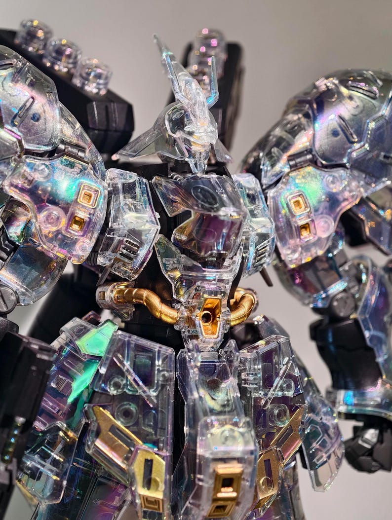 May include: A detailed, clear plastic model of a robot with iridescent accents. The robot features intricate detailing, including gold-colored tubing and panels. The design incorporates sharp angles and a futuristic aesthetic, with a focus on transparency and light refraction.