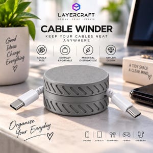 May include: A round, grey cable winder with a textured side pattern and two white USB-C cables extending from opposite sides. The product is labelled with the text Layercraft Cable Winder, Keep Your Cables Neat Anywhere, and Organise Your Everyday.