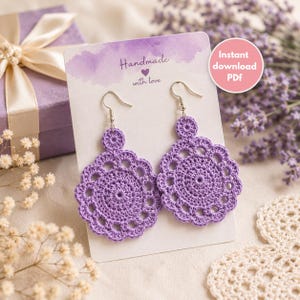 May include: A pair of lavender crochet earrings featuring a circular, scalloped design on a white display card with the text Handmade with love and a pink circle containing the text Instant download PDF, attached to silver-toned metal hooks.