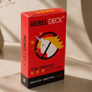 May include: A rectangular red card deck box titled REBEL DECK with a white unicorn graphic inside a black circle with a slash. The text reads DARE, THE ORACLE WITH ATTITUDE, and ZERO FILTER + ZERO F*CKS = ALL FUN, with yellow lightning bolt icons.