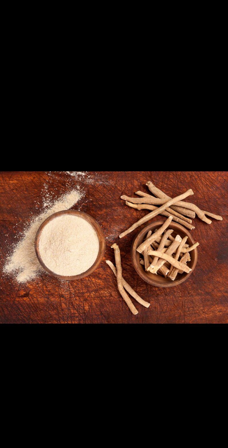 May include: Two small wooden bowls containing ashwagandha. One bowl is filled with a fine, light beige powder, with some spilled on the surface. The other bowl holds several dried, woody, light brown root segments arranged in a cluster.