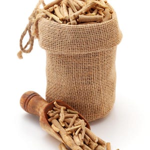 May include: A small, tan burlap drawstring sack filled with light brown, woody root segments. A matching wooden scoop rests in front of the sack, also containing a portion of the same light brown, cylindrical root pieces scattered on the surface.