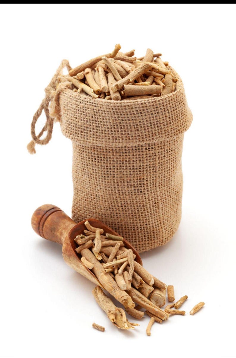 May include: A small, tan burlap drawstring sack filled with light brown, woody root segments. A matching wooden scoop rests in front of the sack, also containing a portion of the same light brown, cylindrical root pieces scattered on the surface.