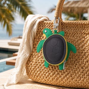 May include: A woven straw tote bag with two rounded handles, featuring a turtle-shaped coin purse attached by a silver metal clip. The turtle accessory has a dark gray textured shell, a bright yellow border, and green limbs and head.