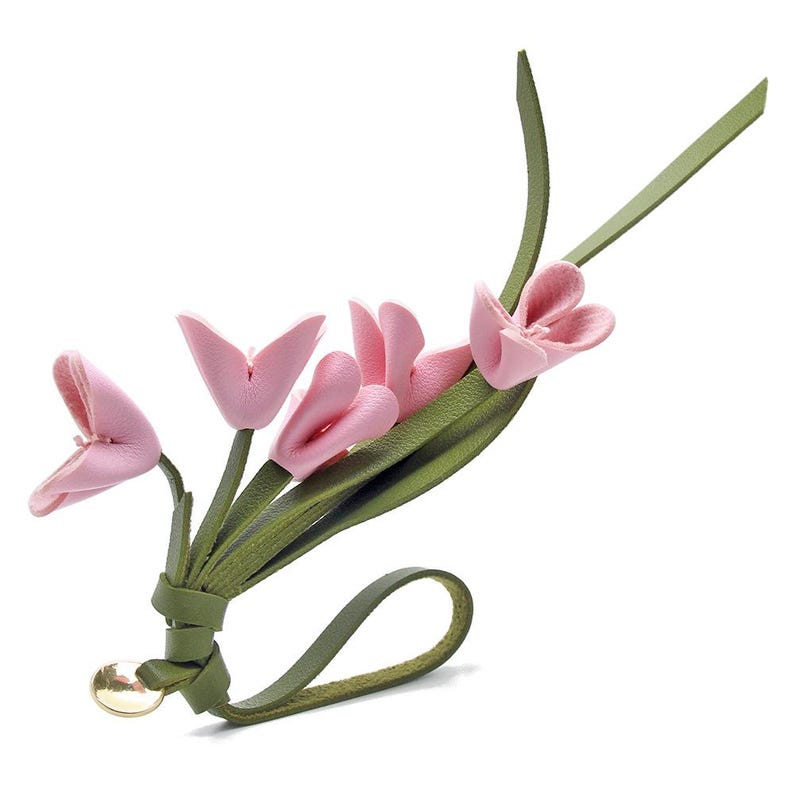 Puede incluir: Un accesorio floral artesanal con p&eacute;talos de flores de cuero rosa y hojas y tallos de cuero verde. El dise&ntilde;o incluye un lazo y un acento met&aacute;lico dorado, creando un aspecto &uacute;nico y elegante. Adecuado para diversos usos.