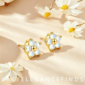May include: A pair of gold stud earrings shaped like flowers, each featuring five iridescent white opal-like petals surrounding a central gold sphere. The text "EASY ELEGANCE FINDS" is printed in white at the bottom of the image.