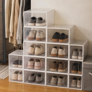 Puede incluir: Una pila de cajas de almacenamiento para zapatos de plástico transparente dispuestas en forma escalonada. Cada contenedor rectangular individual contiene un par de zapatillas o zapatos casuales, con una puerta frontal y orificios de ventilación.