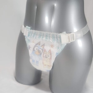 May include: A disposable diaper featuring a cartoon design, secured with a clear, adjustable belt. The diaper has a blue and white pattern with cartoon characters. The belt has white plastic clasps.