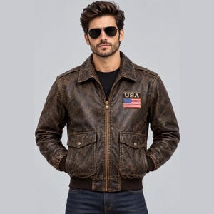 May include: A brown distressed leather bomber jacket featuring a front zipper closure, a fold-down collar, ribbed cuffs and hem, and two front flap pockets. A rectangular patch on the chest displays the text USA above a United States flag.