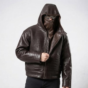 May include: A dark brown jacket with a crocodile skin texture, featuring a built-in hood and a high-neck face covering that zips up to the nose. The garment includes a full-length front zipper and is paired with dark pants.