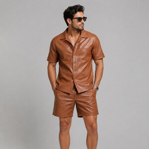 Pode incluir: Um conjunto de camisa de manga curta com botões e calções a condizer, feito de um material liso semelhante a couro. A camisa apresenta um colarinho clássico, uma carcela de botões frontal e dois bolsos no peito.