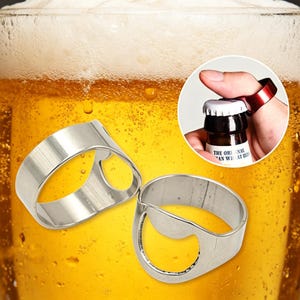 Può includere: Due apribottiglie a forma di anello in metallo color argento con un design a fascia larga. Un anello è mostrato in un riquadro circolare, indossato su un dito mentre rimuove un tappo metallico da una bottiglia di vetro. Superficie liscia.