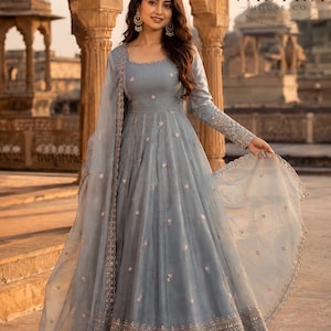 May include: A floor-length grey anarkali dress featuring long sleeves, a round neckline, and a matching sheer dupatta. The garment is adorned with small metallic floral embroidery throughout and a wide, intricate metallic border at the hemline.