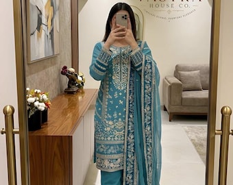 Puede incluir: Un conjunto de tres piezas en color azul cerceta que consta de una túnica de manga larga, pantalones de corte recto y un dupatta a juego. La túnica presenta un intrincado bordado en dorado y blanco a lo largo del escote, los puños y el dobladillo.