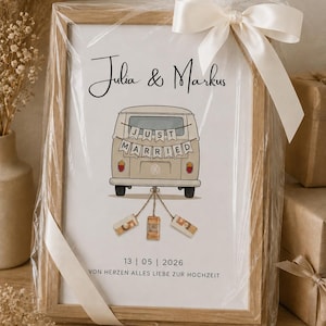 Peut inclure: Une impression encadr&eacute;e dans un cadre en bois clair, emball&eacute;e dans du plastique transparent avec un ruban blanc. L'impression pr&eacute;sente les noms Julia & Markus, une illustration de van beige avec une banni&egrave;re Just Married et la date 13 | 05 | 2026.