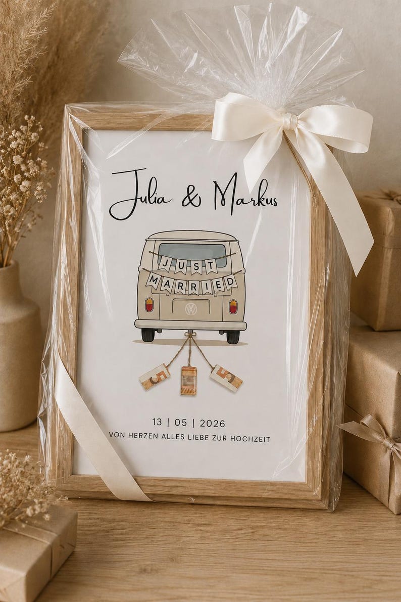 Peut inclure: Une impression encadr&eacute;e dans un cadre en bois clair, emball&eacute;e dans du plastique transparent avec un ruban blanc. L'impression pr&eacute;sente les noms Julia & Markus, une illustration de van beige avec une banni&egrave;re Just Married et la date 13 | 05 | 2026.