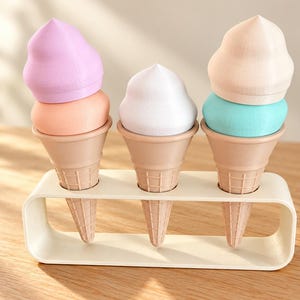 Op de afbeelding: Drie speelgoedijshoorntjes in een crèmekleurige rechthoekige standaard. Het linker hoorntje heeft een lavendelkleurige en perzikkleurige bol, het midden een witte bol en rechts een beige en turquoise bol. Elk hoorntje heeft een wafelpatroon.