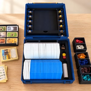 Op de afbeelding: Een blauwe opbergkoffer voor bordspellen met witte en blauwe kaartspellen, een gele en rode dobbelsteen, en kleine zwarte bakjes gevuld met rode, witte, oranje, blauwe, bruine en talingkleurige spelstukken en losse kaarten.