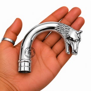 May include: A polished silver-toned metal cane handle featuring a sculpted wolf head design at the end. The curved handle has a smooth, reflective surface and includes a circular logo with the text BE EMPIERS printed on the side of the shaft.