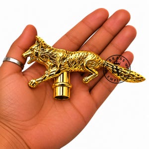 Può includere: Un pomello per bastone in metallo color oro a forma di volpe in corsa, con dettagliata texture del pelo e bocca aperta. Il pomello presenta un punto di attacco cilindrico alla base e un timbro circolare con la scritta BRASS EMPIRE.