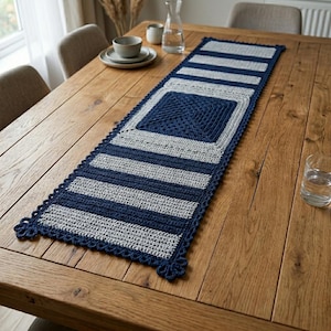 May include: A handmade, rectangular table runner with a crochet design. The runner features alternating stripes of navy blue and light gray. A square of navy blue crochet is in the center. The edges are scalloped with navy blue crochet.