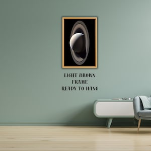 May include: A rectangular wall art print featuring a high-contrast image of the planet Saturn with its prominent rings against a deep black background, encased in a light brown frame with the text LIGHT BROWN FRAME READY TO HANG below it.