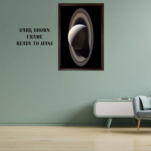 May include: A framed wall art print featuring a detailed image of the planet Saturn with its prominent rings against a black background. The artwork is enclosed in a dark brown frame. The text "DARK BROWN FRAME READY TO HANG" is visible.
