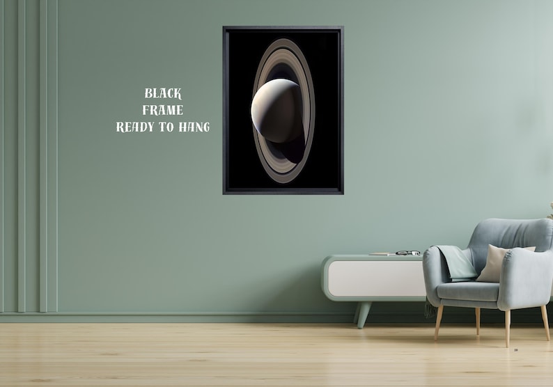 May include: A framed wall art print featuring a vertical depiction of the planet Saturn with its prominent rings against a solid black background. The artwork is enclosed in a thin black frame and includes the text BLACK FRAME READY TO HANG.