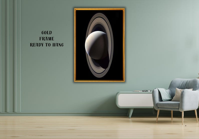May include: A rectangular wall art piece featuring a high-contrast image of a planet with prominent rings set against a black background, enclosed in a thin gold frame. The text GOLD FRAME READY TO HANG is printed in black on the wall nearby.