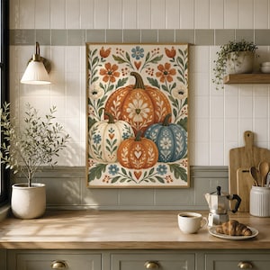 May include: A rectangular wall art print featuring a central illustration of four pumpkins in orange, cream, and blue, decorated with white floral and heart patterns, surrounded by a symmetrical arrangement of green leaves, orange flowers, and blue blossoms.