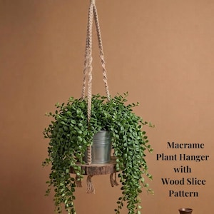 Peut inclure: Un macramé porte-plante avec un motif de tranche de bois. Le porte-plante comprend une corde de suspension, une étagère en bois et un pot en métal rempli de plantes vertes. Le texte "Macramé Porte-Plante avec Motif Tranche de Bois" est visible.
