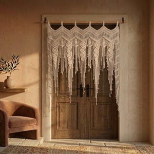 Peut inclure: Un rideau de porte en macramé beige est suspendu devant une porte en bois. Le rideau présente un motif géométrique avec de longues franges pendantes. La porte est en bois et possède des poignées noires. Une chaise et un vase avec des plantes sont visibles.