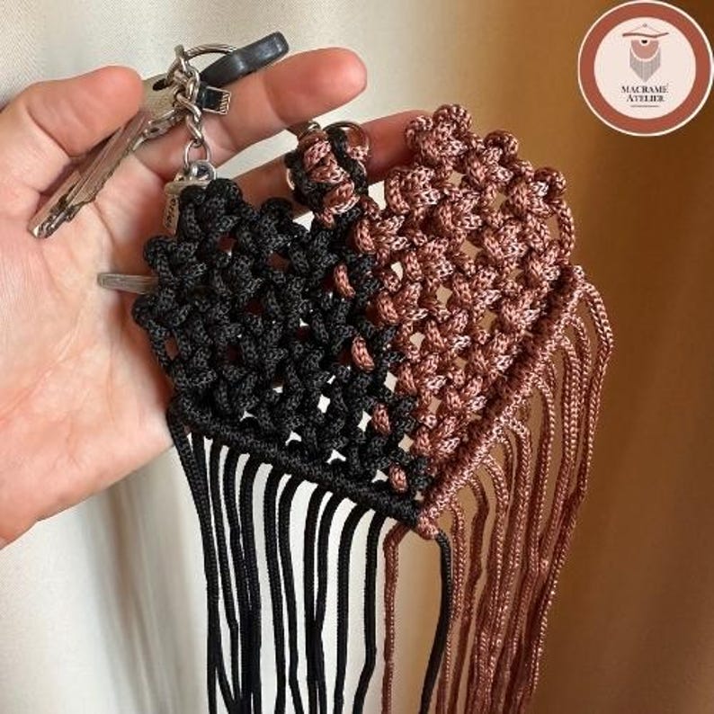 Puede incluir: Un llavero de macram&eacute; en forma de coraz&oacute;n con un dise&ntilde;o dividido, una mitad en cord&oacute;n negro y la otra en cord&oacute;n de color cobre met&aacute;lico. La pieza incluye una anilla met&aacute;lica y largos flecos de cord&oacute;n colgantes en el borde inferior.