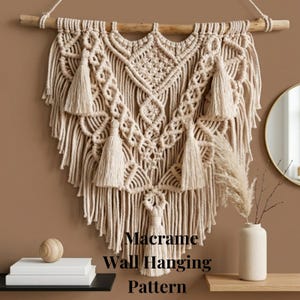 Può includere: Un motivo di arazzo da parete in macramè beige con un tassello di legno. L'arazzo da parete presenta nodi intricati e nappe decorative. Il testo "Macrame Wall Hanging Pattern" è visualizzato nella parte inferiore dell'immagine.