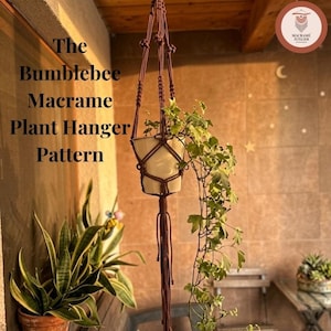 May include: A brown macrame plant hanger holding a white pot with a trailing green ivy plant. The text "The Bumblebee Macrame Plant Hanger Pattern" is visible on the left side, and a circular logo is in the top right corner of the image.