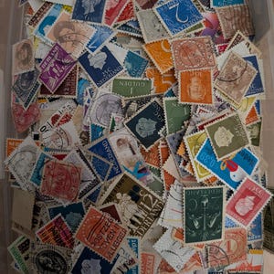 Op de afbeelding: Een grote verzameling vintage postzegels uit Nederland, met een verscheidenheid aan kleuren, vormen en ontwerpen. De postzegels tonen portretten, numerieke waarden en de tekst Nederland, wat diverse historische poststempels laat zien.