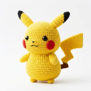 Może przedstawiać: Ręcznie robiona żółta szydełkowa lalka Pikachu z czarnymi oczami, czerwonymi policzkami i zygzakowatym ogonem. Uszy mają czarne końcówki. Urocza, miękka zabawka.