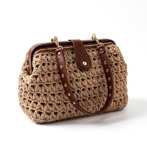 Könnte beinhalten: Eine beige gehäkelte Handtasche mit einer strukturierten Rahmenöffnung, einem dunkelbraunen Ledergriff und einem zentralen Lederverschluss. Die Tasche ist aus dickem, strukturiertem Garn in einem offenen Webmuster mit goldfarbenen Metallbeschlägen gefertigt.