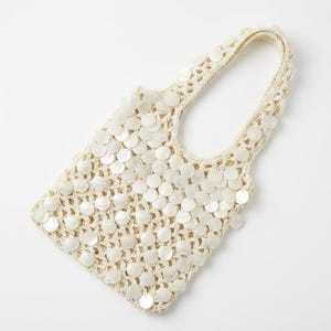 May include: Cream-coloured crochet tote bag decorated with numerous round, iridescent shell-like embellishments. The bag has a rectangular body and a handle, with a delicate, open-weave design. Suitable for carrying small items.