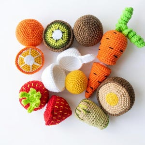 May include: A collection of crocheted play food items including a whole orange, a sliced orange, a kiwi slice, a brown sphere, a carrot with green tops, a white egg shell with a yellow yolk, a red strawberry, and a sliced brown vegetable.