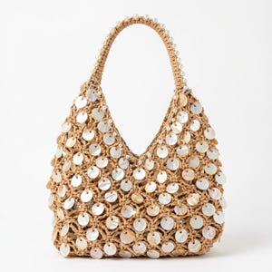 Könnte beinhalten: Eine beige gewebte Hobo-Tasche mit einer häkelartigen Struktur, die mit zahlreichen runden, irisierenden Muschelscheiben verziert ist. Der einzelne Schulterriemen ist entlang der Oberkante mit einer Reihe kleiner weißer Perlen besetzt.