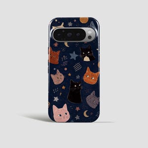 May include: A dark blue smartphone case featuring a repeating pattern of various cat faces in shades of orange, black, gray, and pink, interspersed with small yellow and blue stars, crescent moons, and abstract white line markings.
